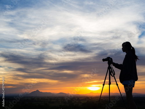 Silhouette of woman shooting with camera at sunset