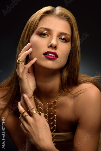 Fashion photo of attractive young blonde woman with styled make–up, long necklace and many rings on her fingers