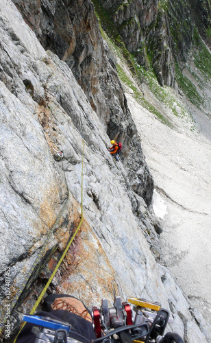 a rock climber on a steep rock face in the Swiss Als with a mountain guide belaying him in the foreground