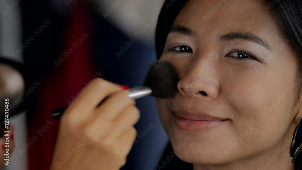 A young beautiful Asian woman having makeup applied, the makeup artist is applying blush or foundation with a brush. A young beautiful Asian woman having makeup applied, the makeup artist is applying blush or foundation with a brush.
