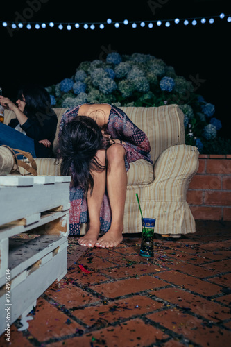 Young drunk woman holding her head sitting in the sofa in a outdoors party. Fun and alcohol and drugs problems concept.