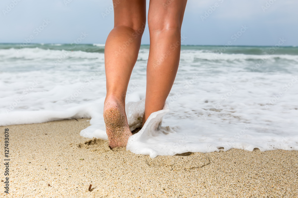 Closeup of a man's bare feet walking at a beach, with a wave's e Closeup of a man's bare feet walking at a beach, with a wave's e