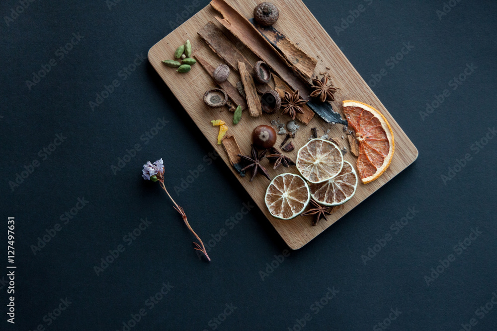 Cutting board with mixed spices and dry citrus slices . On the black background with one desiccated flower on the left side. Cutting board with mixed spices and dry citrus slices . On the black background with one desiccated flower on the left side.