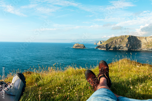 couple in love watching a beautiful view over the ocean. View of the legs on the landscape background sky and bay tintagel castle ruins
