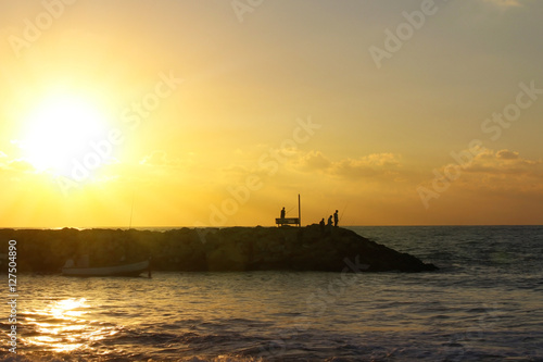 Silhouettes of fishermen at sunset. Rocky shore for fishing. Evening sky and quiet sea background. © MZalevsky