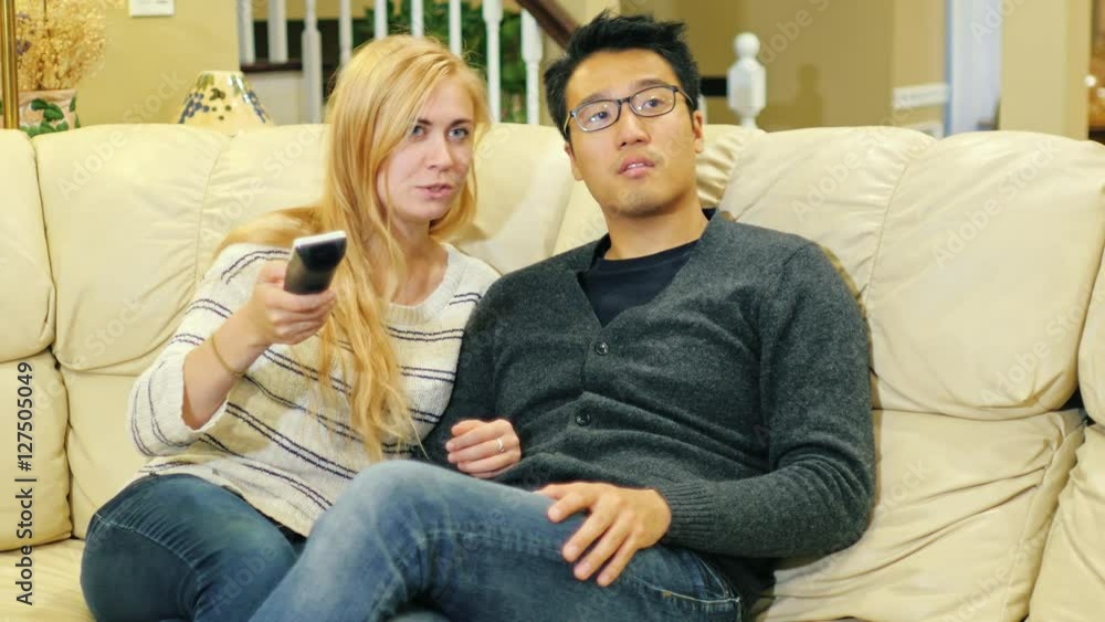 Friends watching television in the living room. Korean man and Caucasian woman. Keep the remote in hand Friends watching television in the living room. Korean man and Caucasian woman. Keep the remote in hand