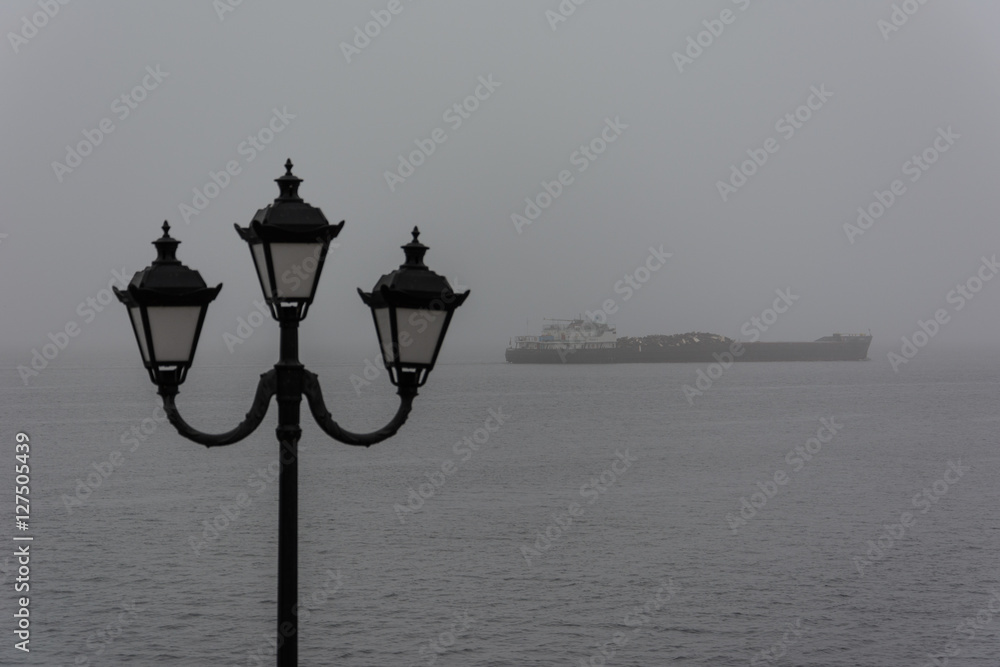 Ship in mist, amid the urban lamp. Fog over the water.