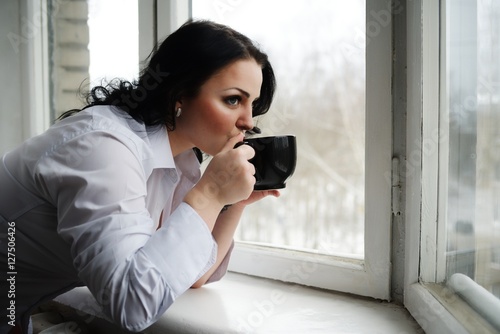 Beautiful girl looks out of window and holds a cup. Winter morning. Free Download Beautiful girl looks out of window and holds a cup. Winter morning. - GFXLoad
