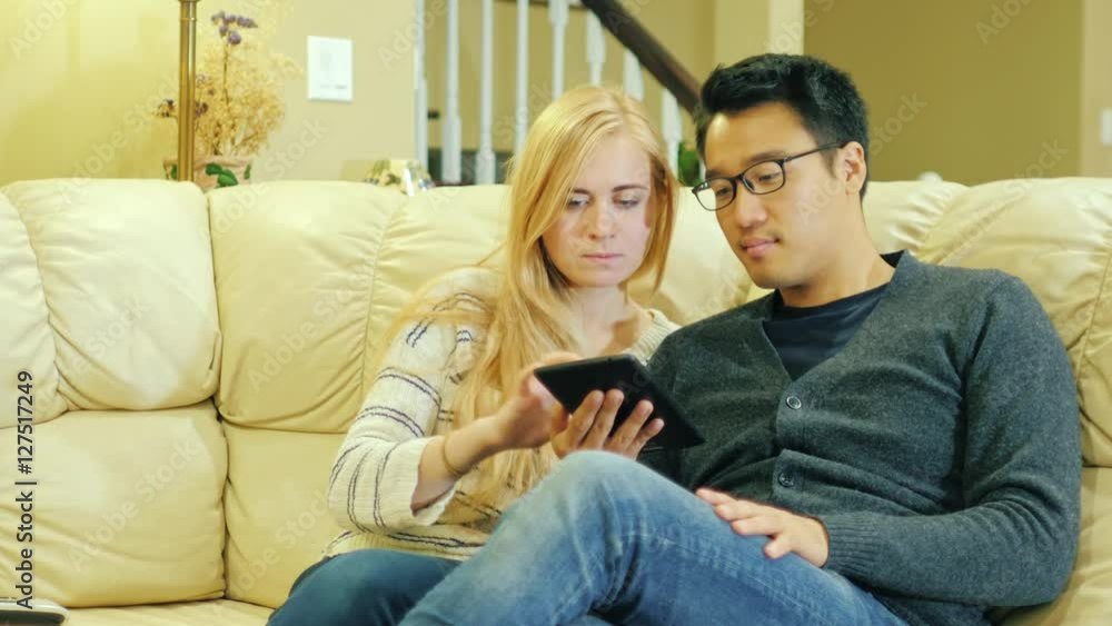 Young multi-ethnic couple relaxing at home, use the tablet. Sit on the couch Young multi-ethnic couple relaxing at home, use the tablet. Sit on the couch