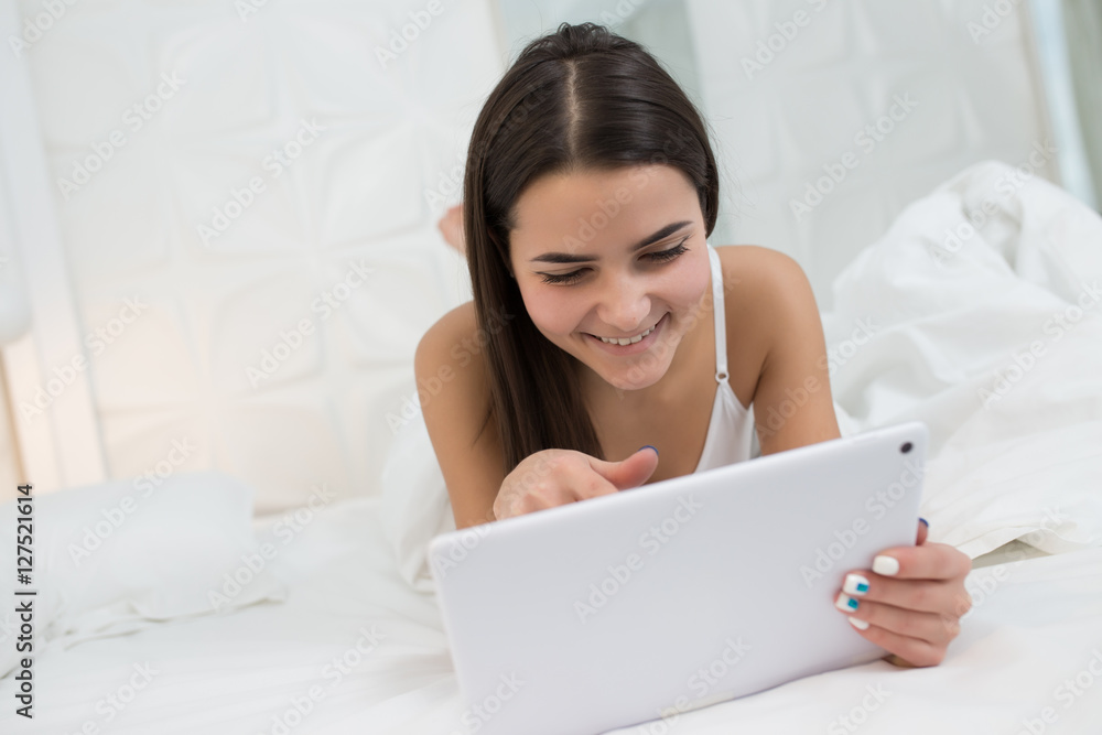 Woman using tablet at the morning. She lies on white bed Woman using tablet at the morning. She lies on white bed