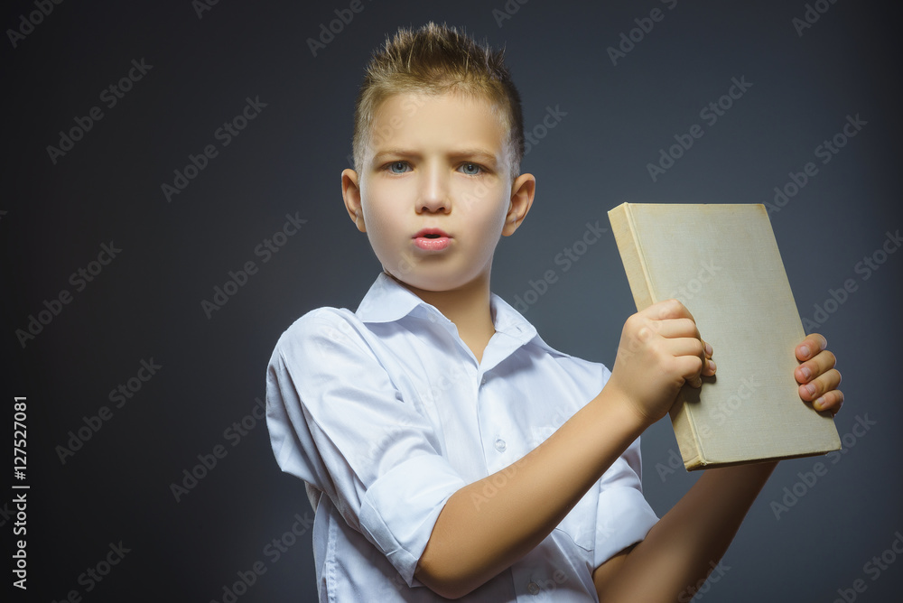 Handsome little stressed boy with book isolated on gray background Handsome little stressed boy with book isolated on gray background