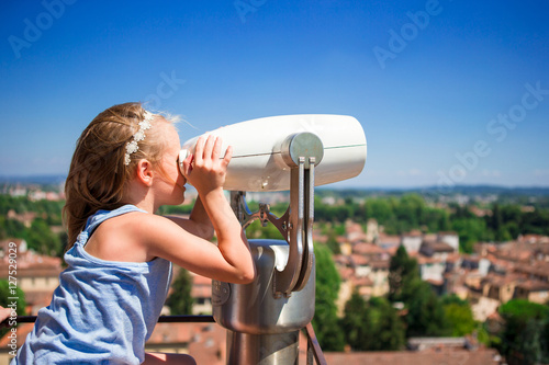 Bilde på lerret Beautiful little girl looking at coin operated binocular on terrace at small tow