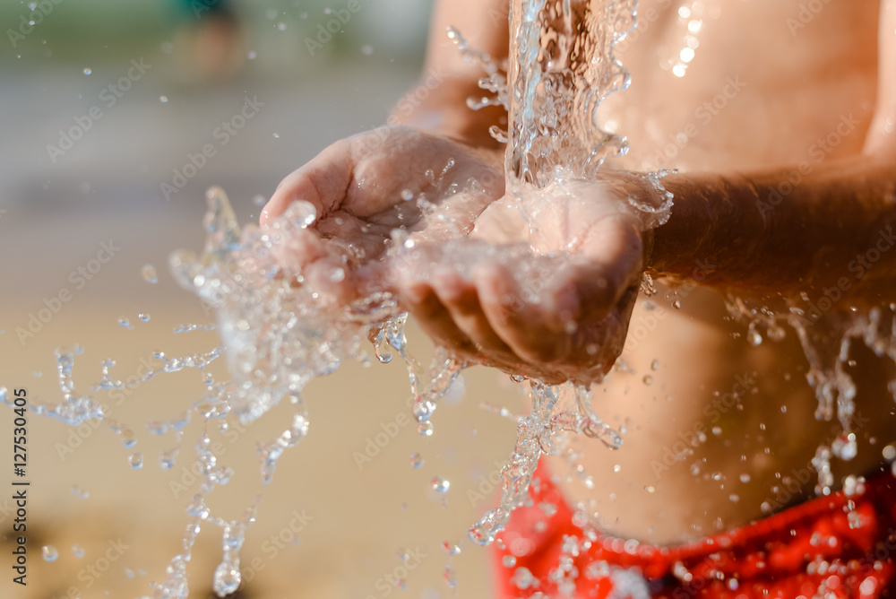 Fototapeta premium Closeup on child hand catching water. Splashing drops on sunny summer outdoors background.