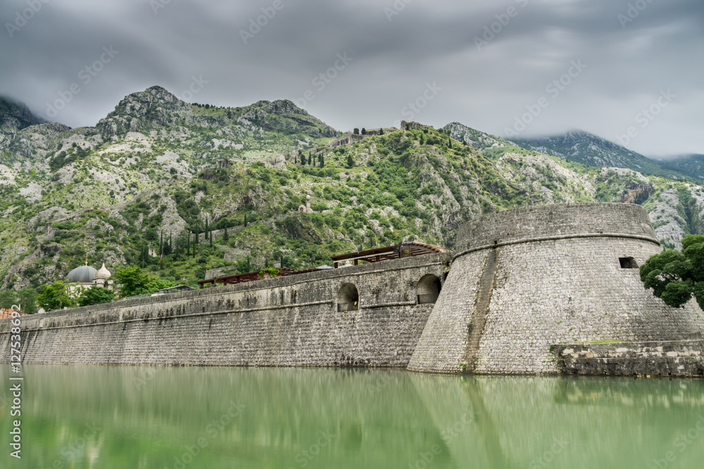 Kampana Tower and Citadel, the World Heritage listed fortifications surrounding the medieval village of Kotor in Montenegro reflected in the Skurda River, with mountains in the background.