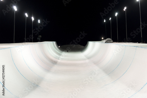Snowboarder in a snow halfpipe at night lit up by lights