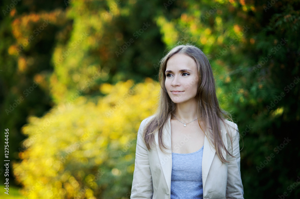 Portrait of beautiful young woman with long brown flowing hair, clothes in business style, easy smile, glance to the side, nature, Sunny day. Portrait of beautiful young woman with long brown flowing hair, clothes in business style, easy smile, glance to the side, nature, Sunny day.