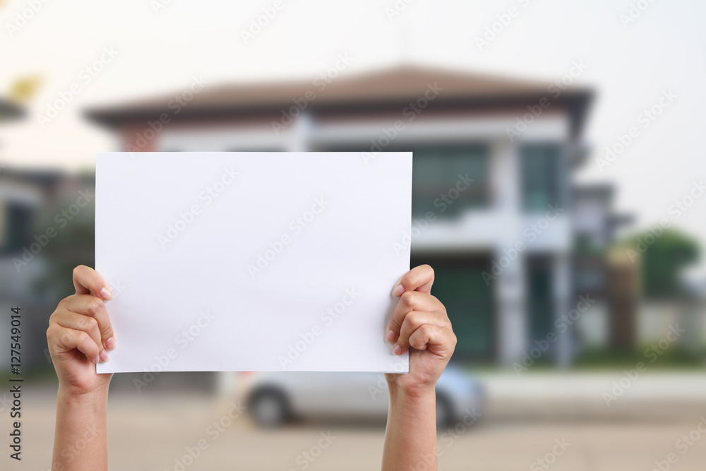 Hand holding blank paper with house background. Hand holding blank paper with house background.