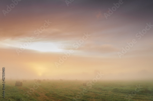 Sunrise over a misty meadow with straw blocks