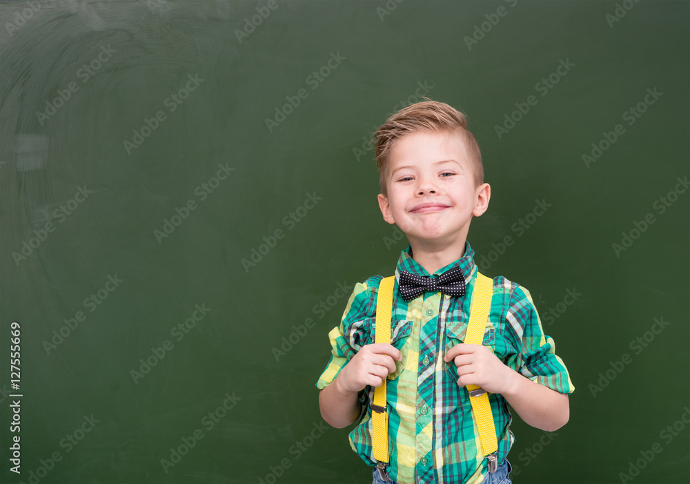Young boy standing near empty green chalkboard