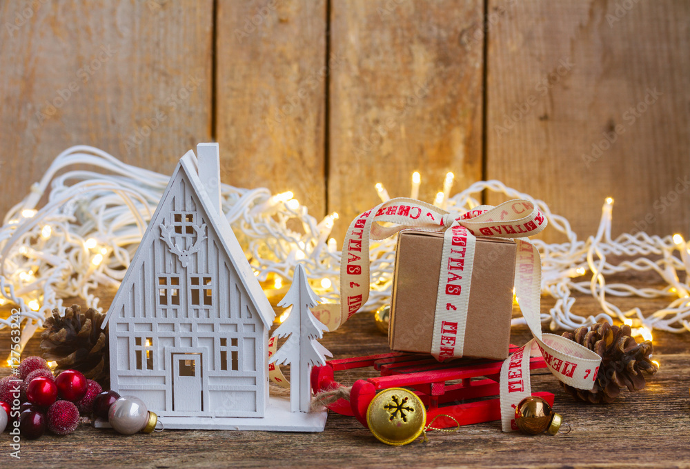 House and gift box on sledge with christmas lights on wooden background