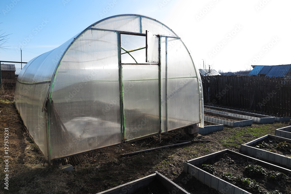 Handmade polycarbonate greenhouse and garden beds in the April garden against a blue sky