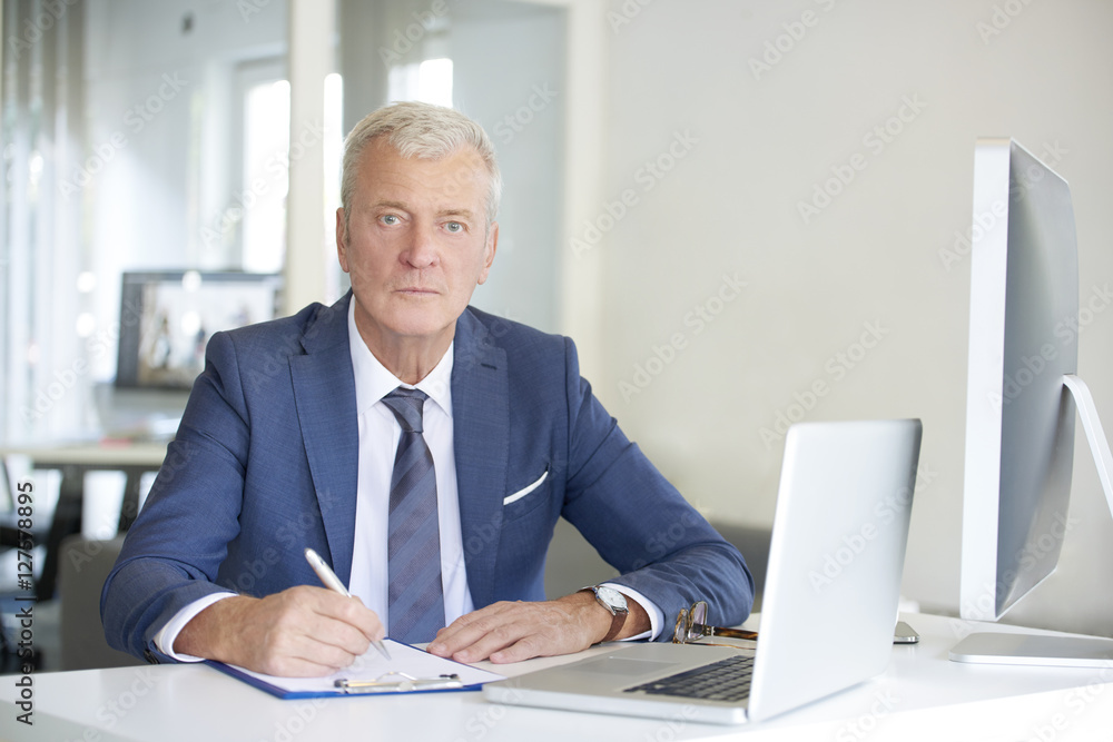 Senior professional man at work. Shot of an old financial businessman sitting at his workstation in front of computer and laptop while doing some paperwork. Senior professional man at work. Shot of an old financial businessman sitting at his workstation in front of computer and laptop while doing some paperwork.
