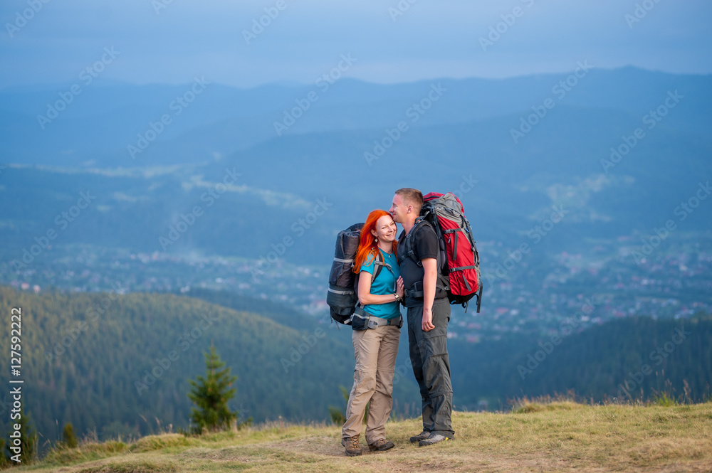 Tourists man and red-haired woman standing facing each other and smiling on the road in the mountain on the background of the landscaped mighty mountains