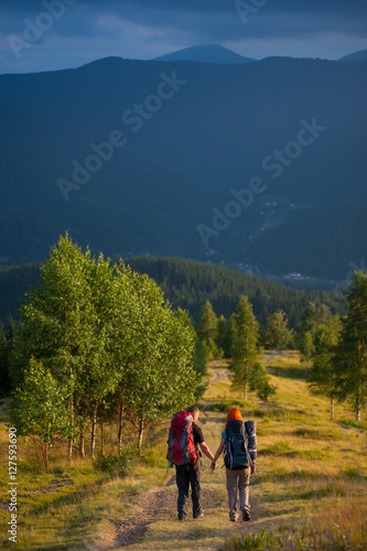 Rear view couple tourists with backpacks walking along a beautiful mountain area holding hands. Lifestyle active vacations concept mountains landscape on background