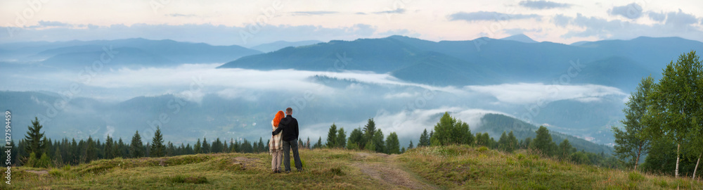 Romantic couple tourists standing on a hill enjoying a morning h