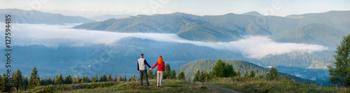 Back view man holding hands red-haired woman standing on a hill,