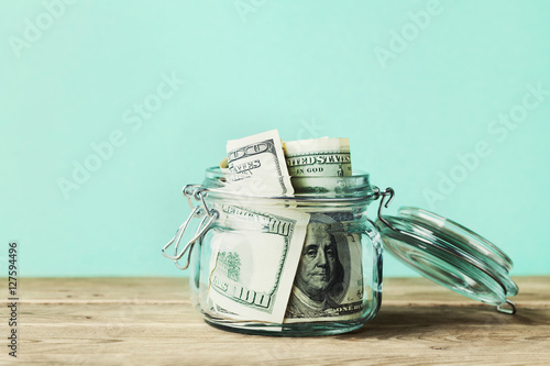 Dollar bills in glass jar on wooden table. Saving money concept. photo