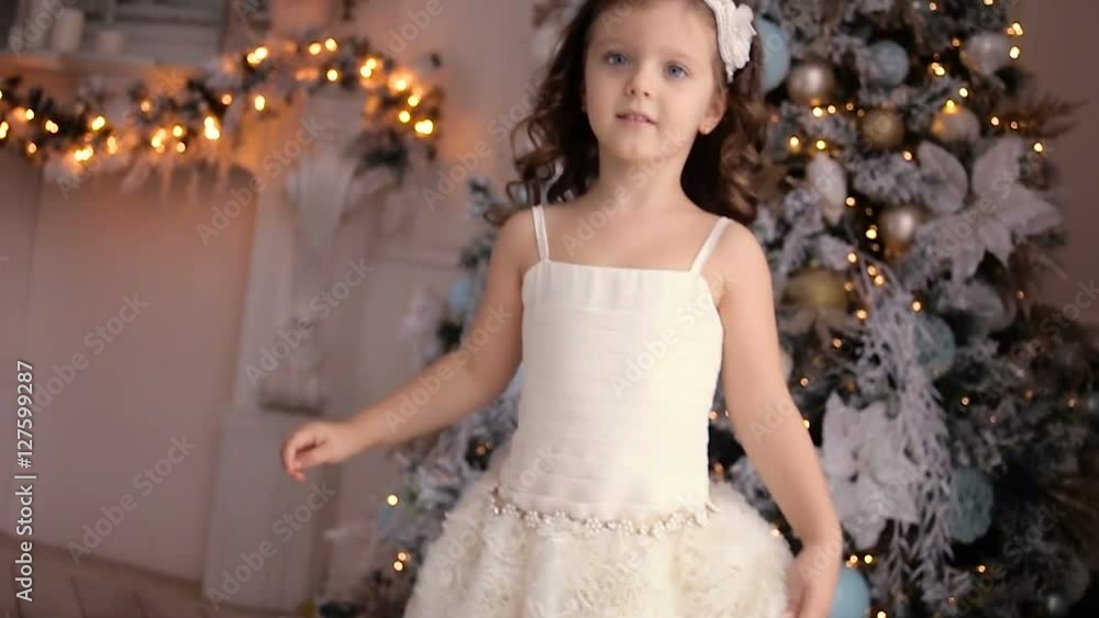 little girl three years old in a white dress dancing around the decorated Christmas tree in room little girl three years old in a white dress dancing around the decorated Christmas tree in room