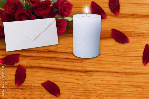 white envelope and burning candle with red rose petals from flower bouquet on wooden board