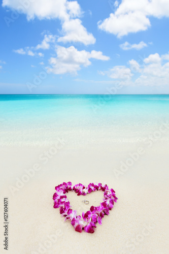 Two wedding rings in a heart lei on beach vacation. Hawaiian flower necklace lying on the sand in the shape of a heart with rings for marriage proposal in tropical vacation destination honeymoon.