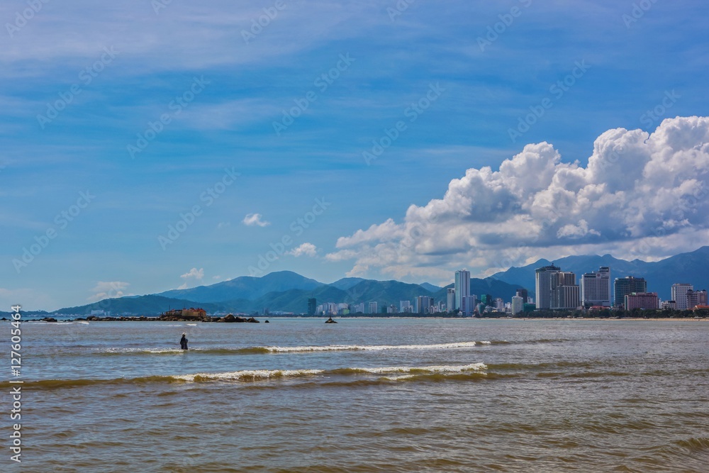 Asian holiday resort Nha Trang bay Vietnam on a beautiful tropical sunny day with a fisherman wading into the south china sea, with the city landscape and mountains in the background.