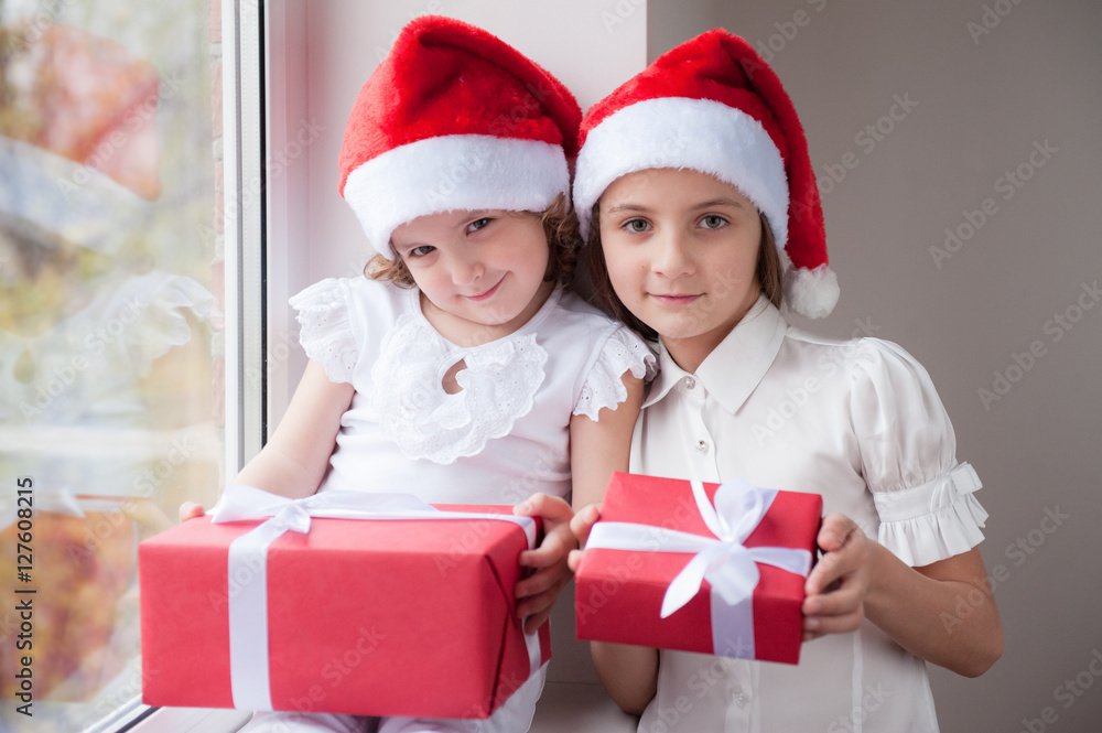 two little sisters in Santa hats holding boxes with gifts two little sisters in Santa hats holding boxes with gifts
