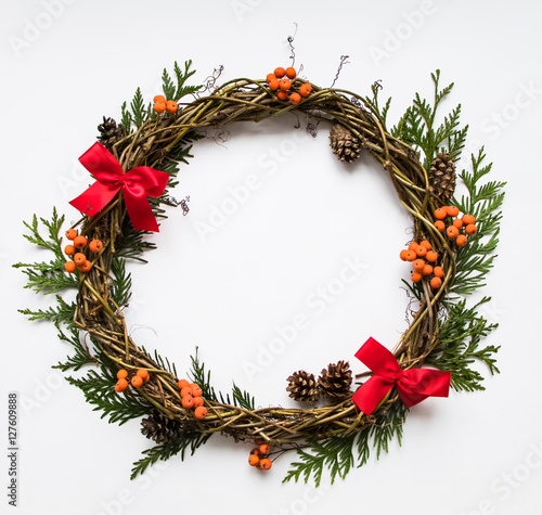 Festive wreath of vines with decorative bows, thuja branches, rowanberries and cones. Flat lay, top view photo