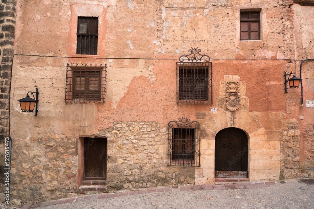 Fachada de un edificio de un pueblo español antiguo con ventanas y puertas varias.