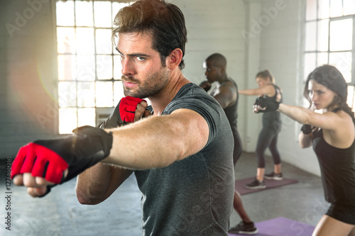 Intense focused man serious expression punching boxing workout throwing fist with group gym