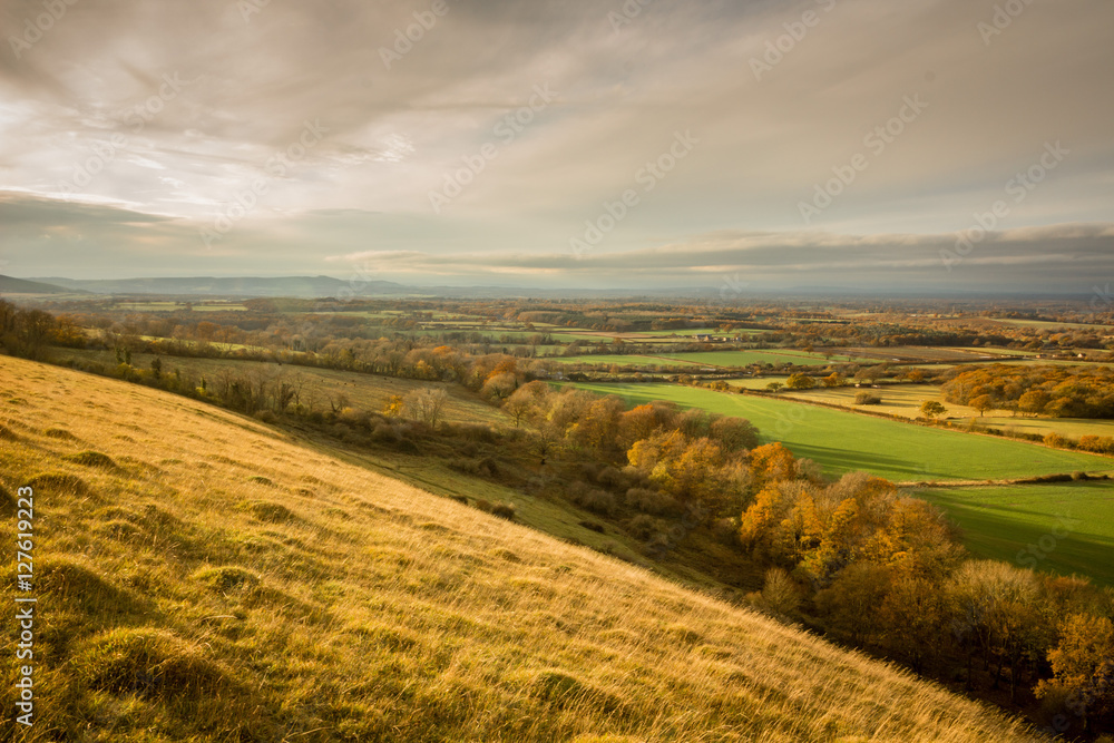 Autumn landscape view from Wolstonbury Hill, South Downs, Sussex, England. Taken close to sunset, looking out across farmland and woodland.