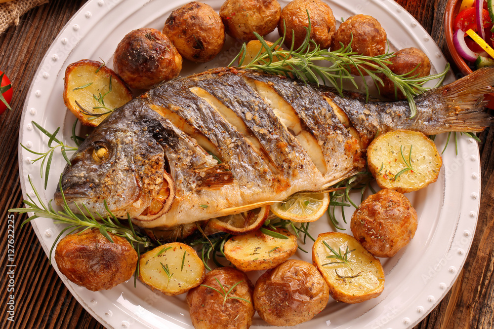 Grilled fish with roasted potatoes and vegetables on the plate Grilled fish with roasted potatoes and vegetables on the plate