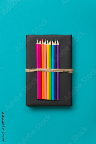 Colorful school and office supplies - pencils and ruler on black book and blue background. Top view with copy space.