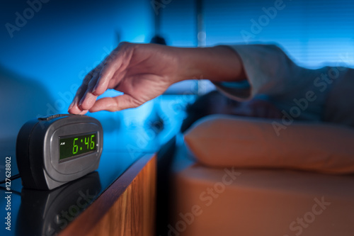 Фотография Woman pressing snooze button on early morning digital alarm clock