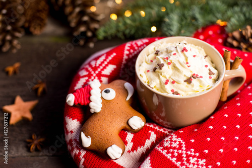 Cup of cocoa with cream and gingerbread against pine branches and traditional knitted sweater. Xmas concept.
