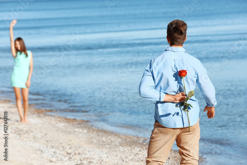 Young man hiding red rose f...