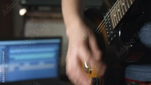 Guitarist playing rhythm on electric guitar and recording session with multitrack recording software on laptop photo