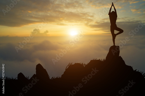 Silhouette young woman practicing yoga on the muontain at sunset