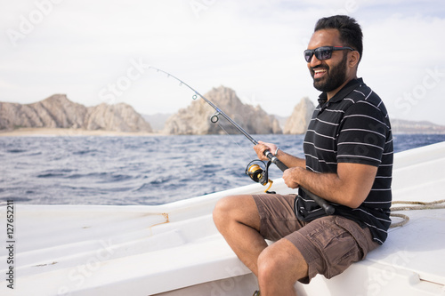 Young East Asian man fishing on open water from the boat. Beautiful sunny day with the shoreline visible in the background.