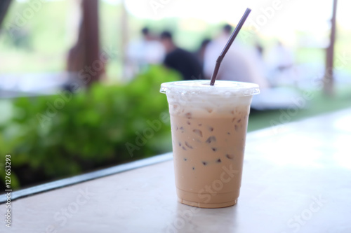 a cup of iced coffee on table with people in a garden at coffee shop blur background