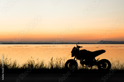 Motorcycle in silhouette at sunset at lake.
